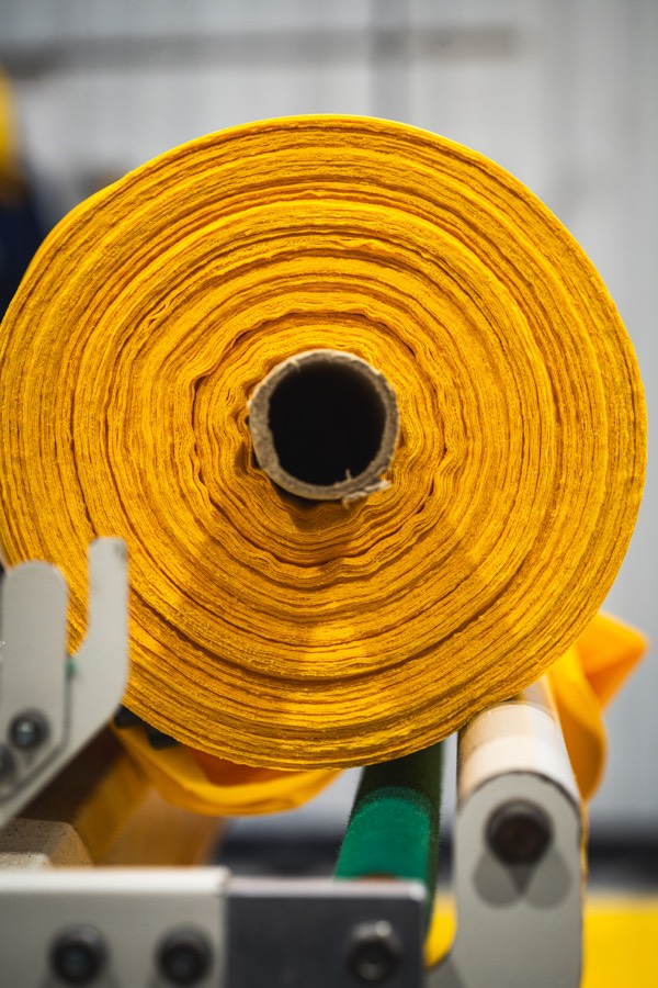 Tecido amarelo sendo processado em máquina de corte industrial
